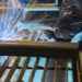 Close-up of a welder safely using a MIG gun to weld together two metal bars.